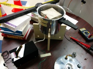 The new high-voltage power supply (black box, lower left) wired into the pressure cooker we are using as a radon exposure chamber. Visible inside the chamber is the nickel-copper anode cap that slides over the copper sample holder.