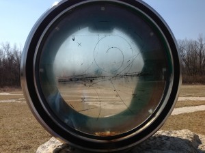 A 30-inch bubble chamber window mounted in a field by the Fermilab Visitor Center. An example bubble chamber image is imprinted on the glass.