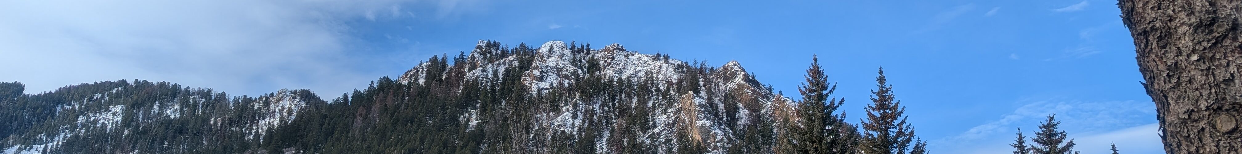 A mountain soars over downtown Aspen, Colorado, on a beautiful winter day. Partly cloudy skies loom above the mountain.