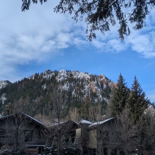 A mountain soars over downtown Aspen, Colorado, on a beautiful winter day. Partly cloudy skies loom above the mountain.