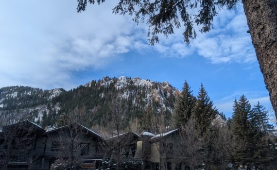 A mountain soars over downtown Aspen, Colorado, on a beautiful winter day. Partly cloudy skies loom above the mountain.