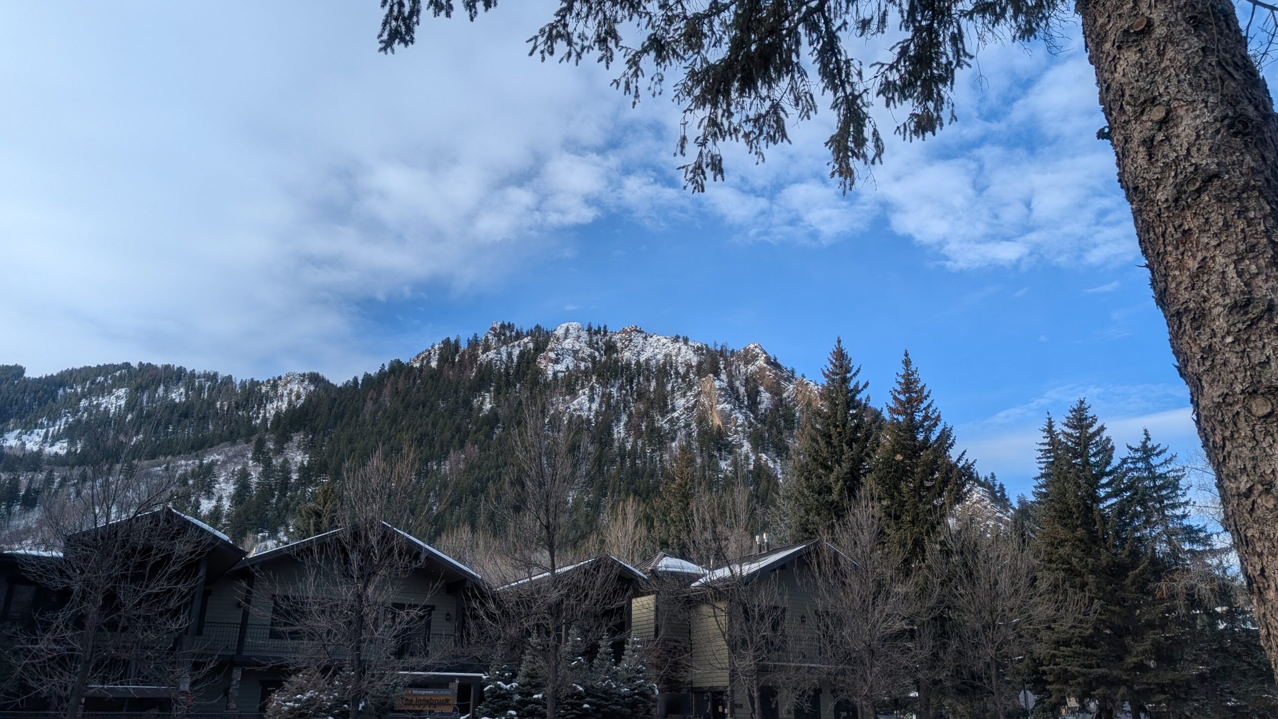 A mountain soars over downtown Aspen, Colorado, on a beautiful winter day. Partly cloudy skies loom above the mountain.