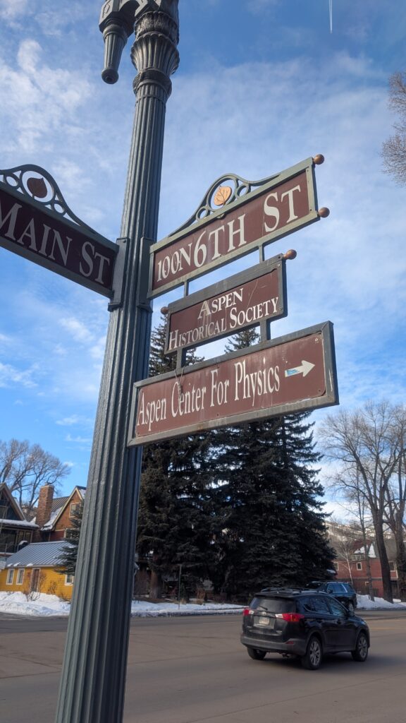 A set of signs indicate directions to key landmarks in an area of Aspen. This includes a sign pointing toward the Aspen Center for Physics.