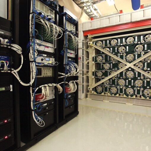 Racks of electronics stand next to and just in front of a large, cube-shaped experiment. The experiment is made from green-painted lead and 128 tubes filled with helium-3.
